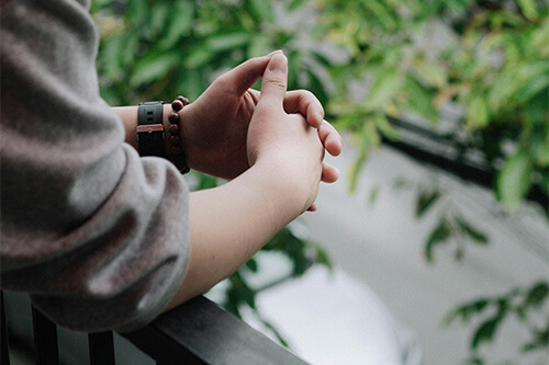 A person holding their hands together while leaning on railing.