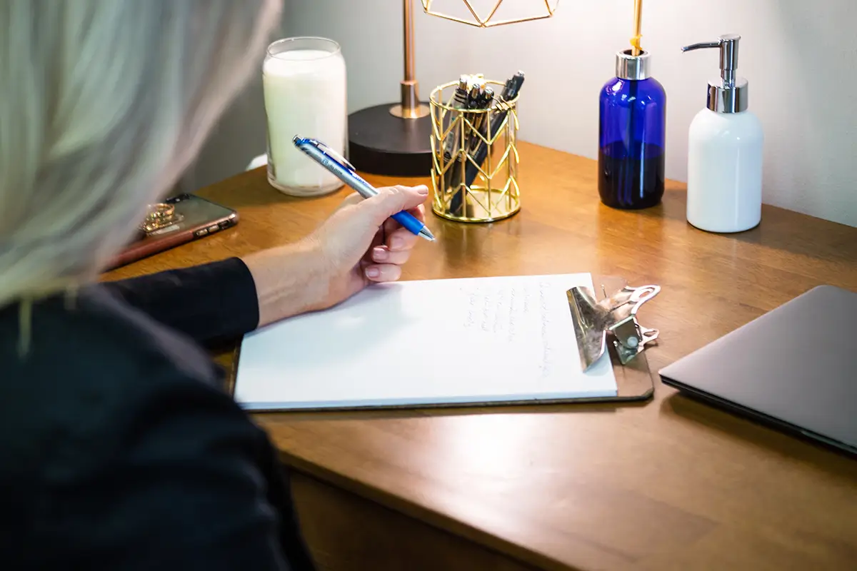 Person writing notes on a clipboard at a desk, in a professional office setting, viewed from behind