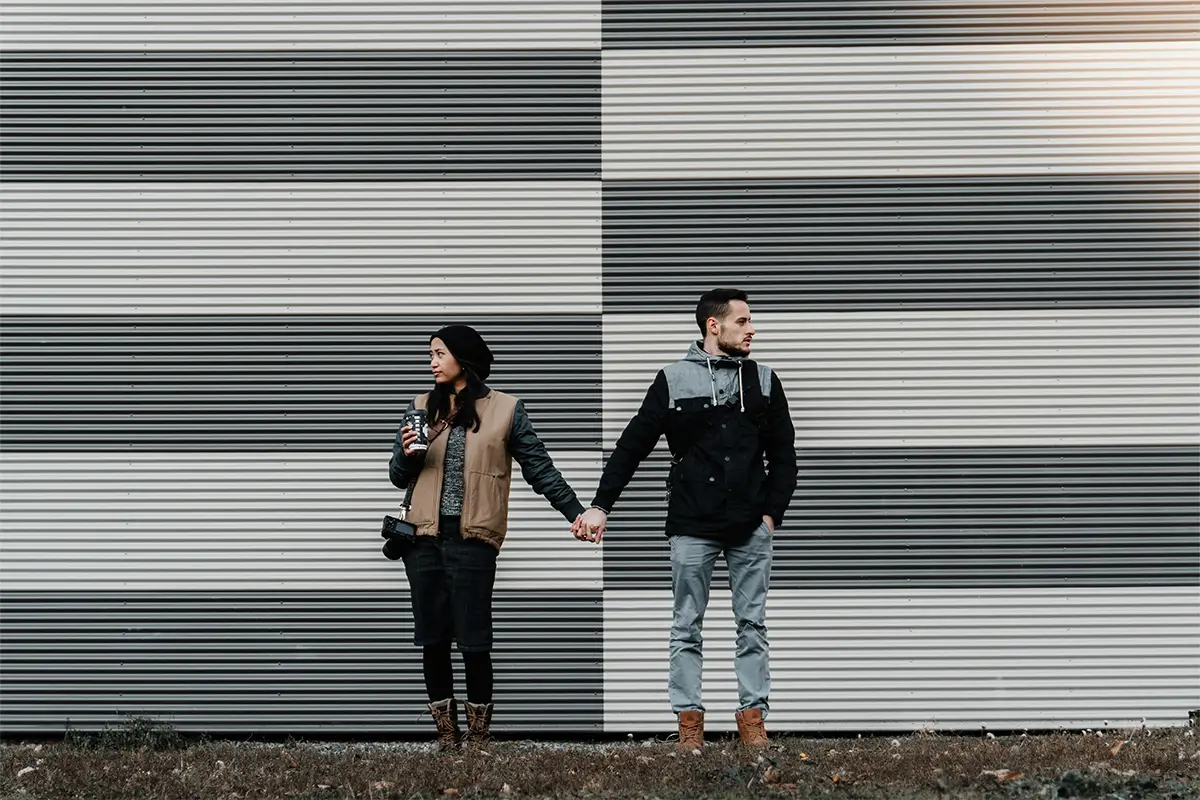 A man and woman holding hands stand in front of a wall with a horizontal black and white striped pattern