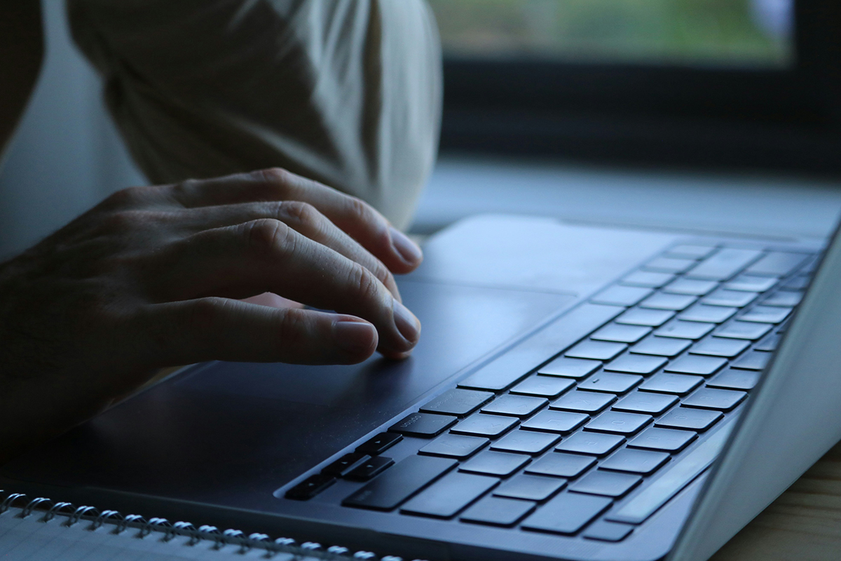 A close-up, low-angle shot of a person's hand using the trackpad of a sleek, dark grey laptop