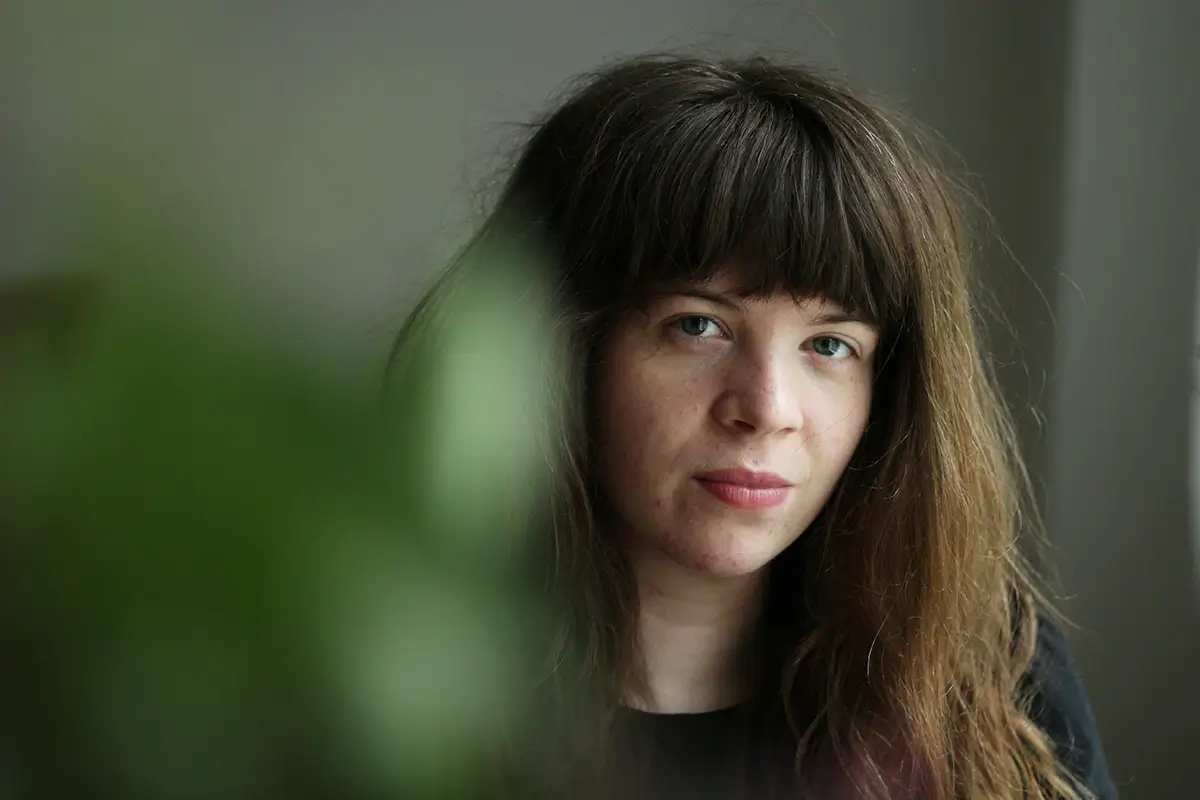 Depression and Dopamine: How They’re Connected Portrait of a woman looking somber and distant, partially hidden behind a blurred plant.